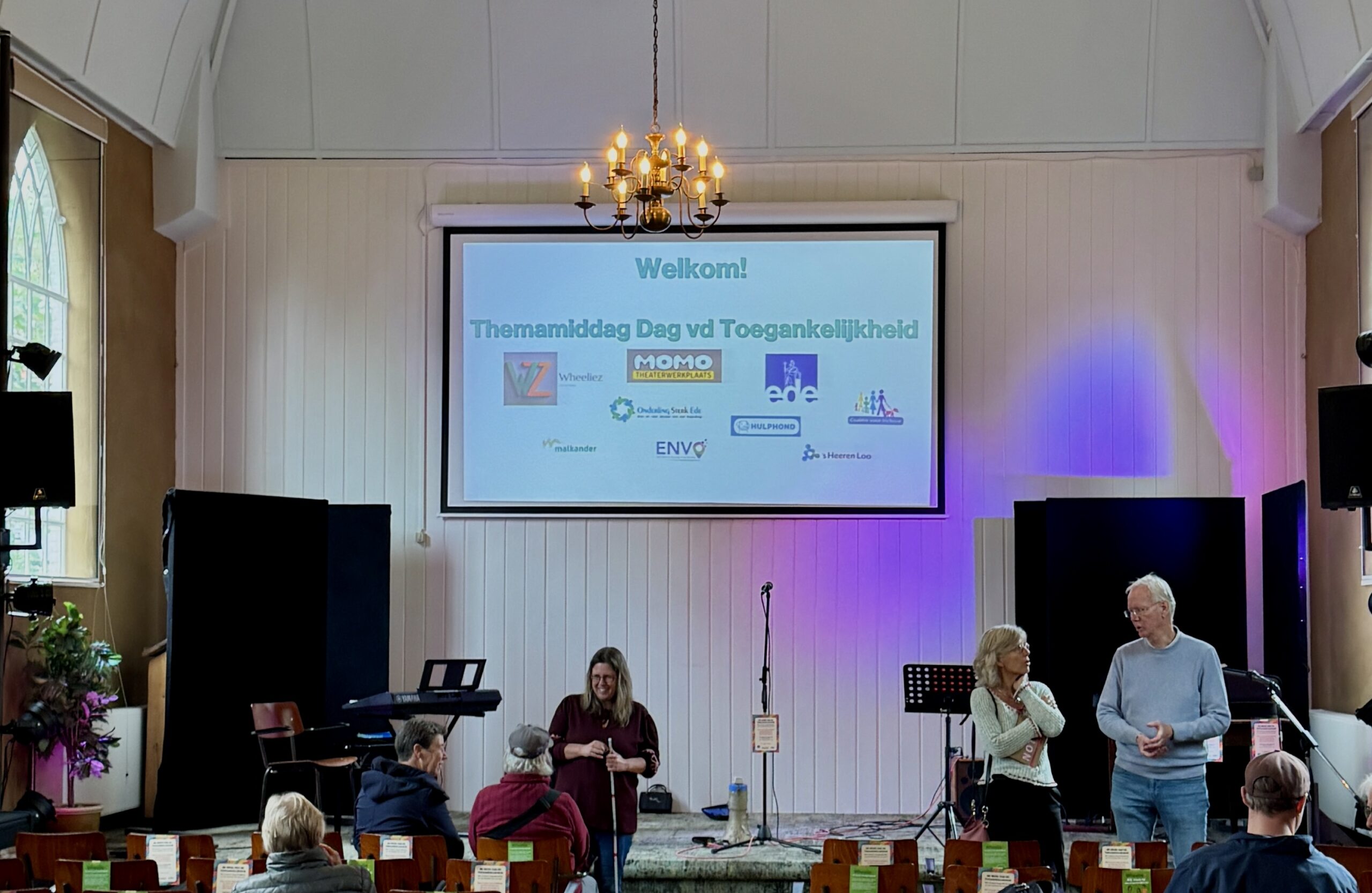 foto van de zaal in Erica Theater met op scherm Welkom en logo's van organisaties waaronder Onderling Sterk Ede
