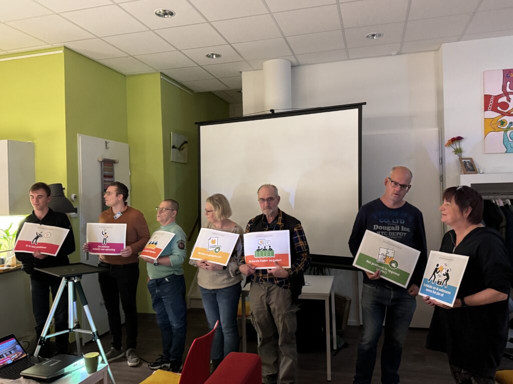 7 deelnemers op een rij met een bordje met teksten als: minister, Tweede Kamer